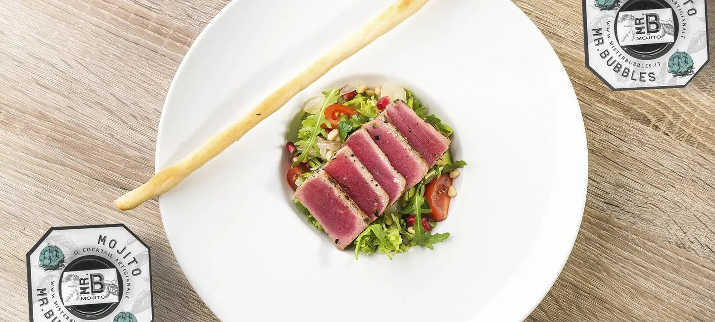 Piatto bianco con tonno scottato su letto di insalata mista colorata e grissino su tavolo legno