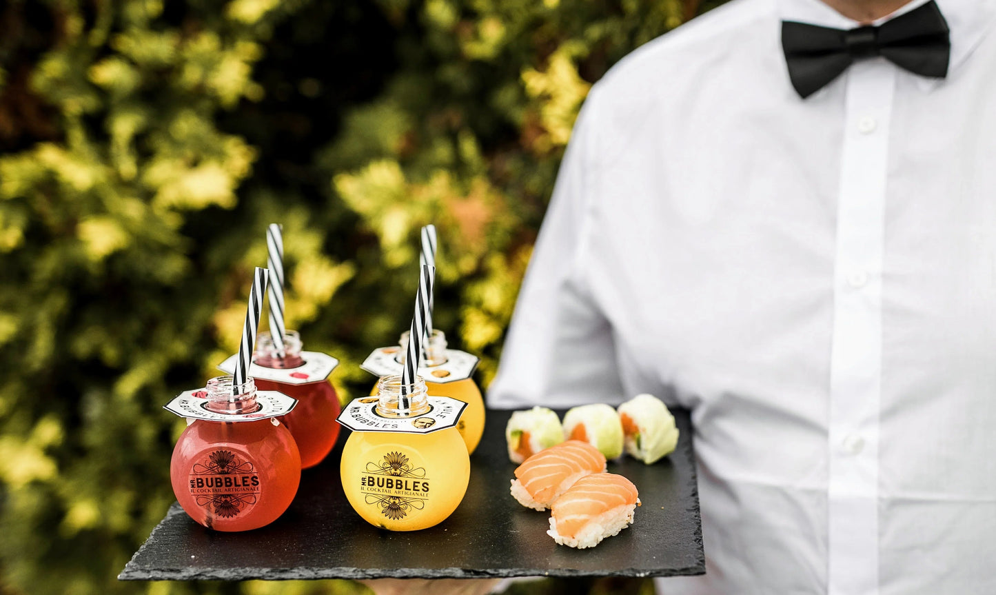 Cameriere in camicia bianca e papillon con vassoio di cocktail artigianali e sushi fresco