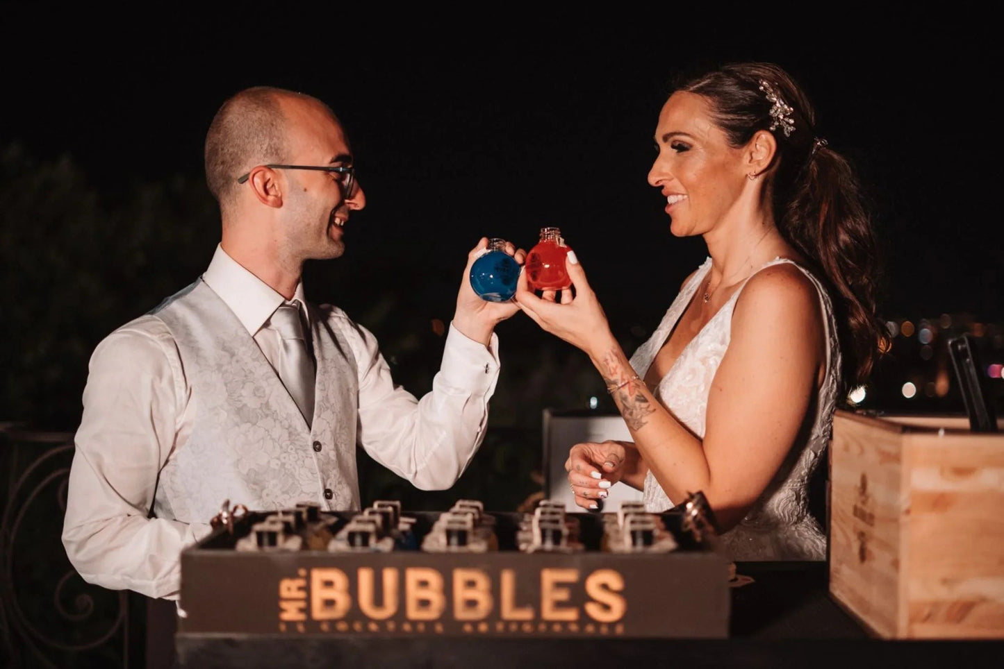 Coppia vestita elegantemente brinda con bottiglie colorate blu e rosso di sera